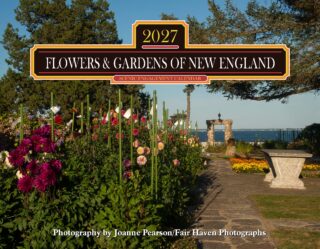 Signboard advertising a 2027 'Flowers & Gardens of New England' calendar, set among colorful garden flowers by a waterfront path.