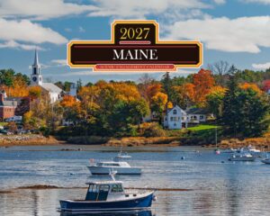 Boats on a calm harbor with autumn trees and a town in the background; a large decorative Maine calendar banner sits across the center.