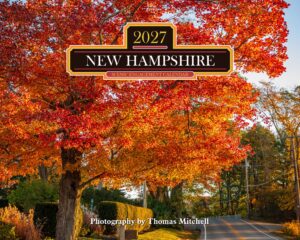 Autumn scene of orange-red maple leaves along a road, with a decorative calendar banner reading 'New Hampshire 2027' and 'Scenic Engagement Calendar' across the center.