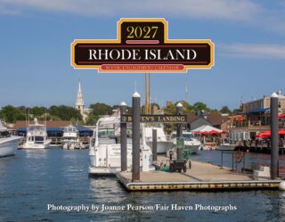 Boat marina with several yachts docked, under a large Rhode Island Scenic Engagement Calendar sign overhead.